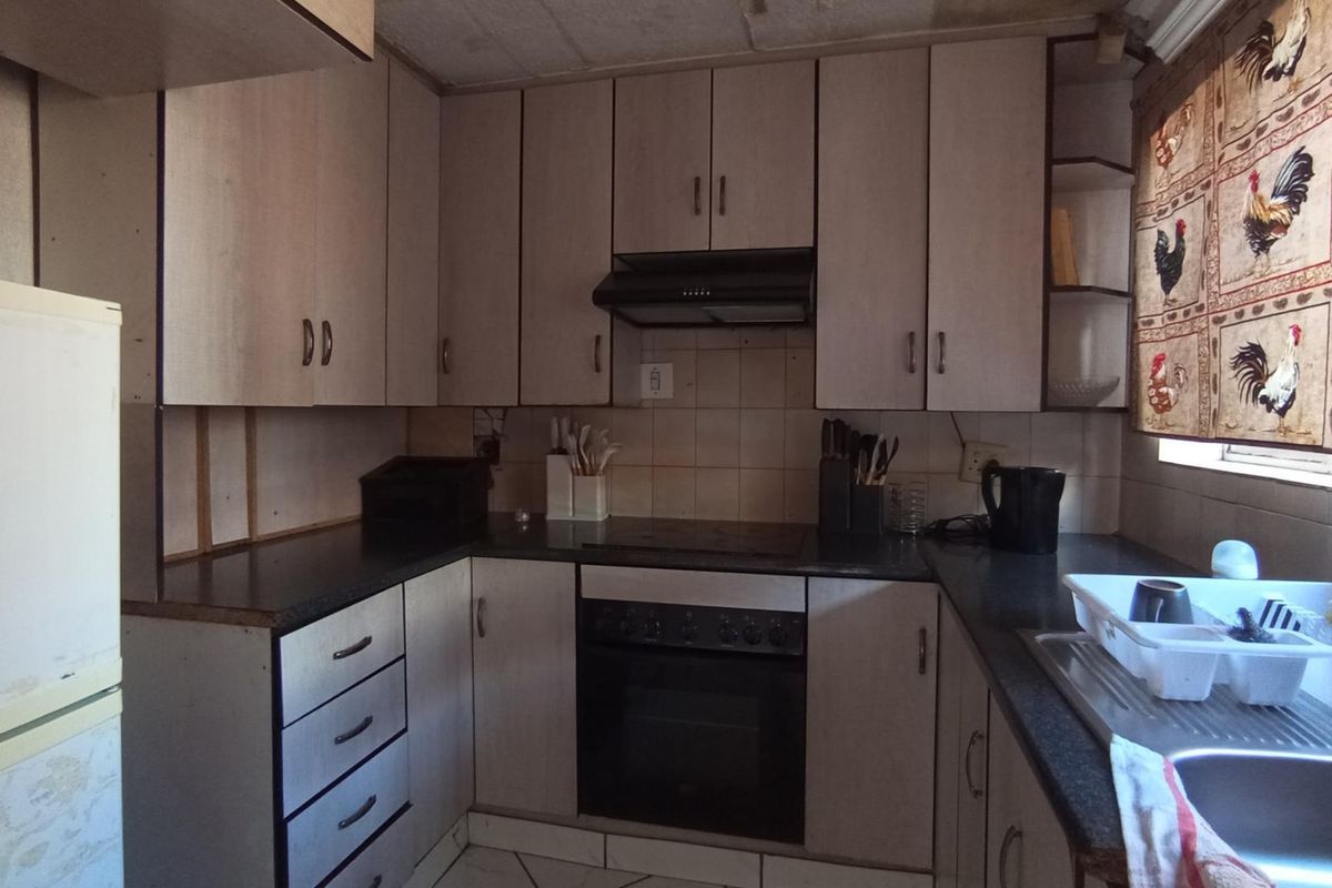 A functional kitchen featuring built-in cabinetry, a built-in oven with extractor fan, and a stainless steel sink, offering potential for modern renovation.