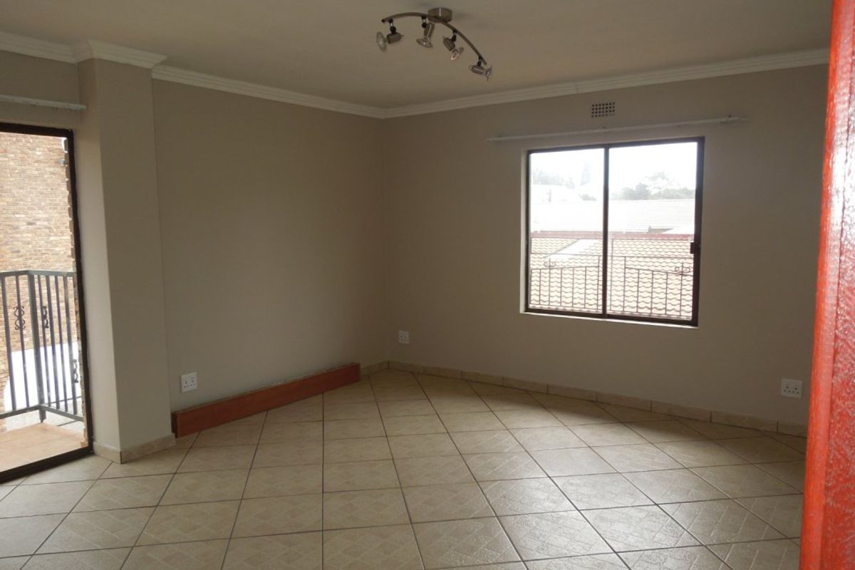 An empty, neutrally painted living room featuring tiled flooring, a ceiling spotlight fixture, and access to a small balcony through a sliding glass door.