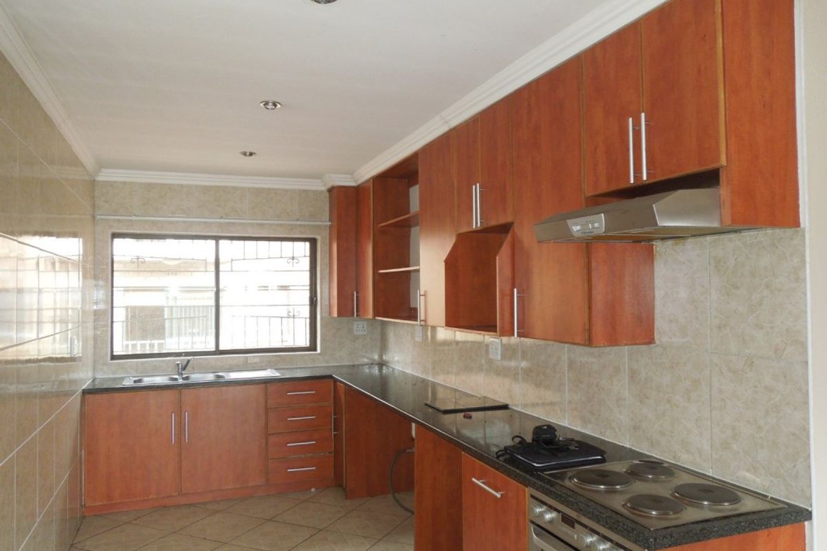 A functional kitchen featuring laminate cabinetry, granite countertops, a built-in oven with hob, and tiled finishes throughout.