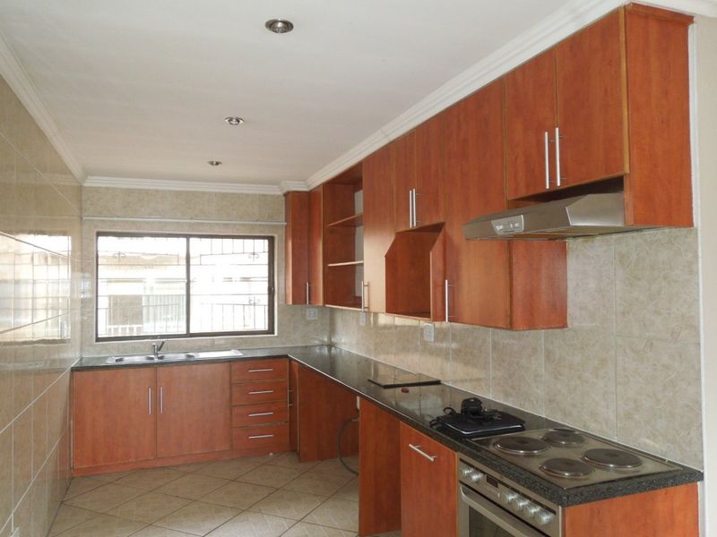 A functional kitchen featuring laminate cabinetry, granite countertops, a built-in oven with hob, and tiled finishes throughout.