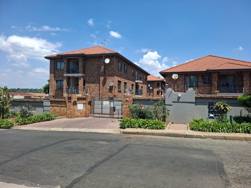 Front exterior view of a multi-story face brick townhouse complex featuring tiled roofs, secure gated entrance, and perimeter electric fencing.