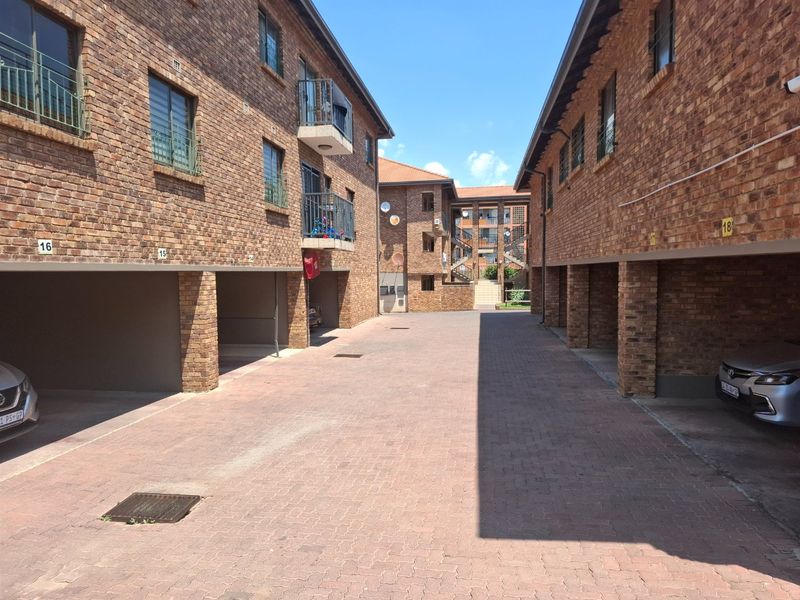 A view of the townhouse complex driveway featuring face brick facades, undercover parking bays, and access to upper-level units via external staircases.