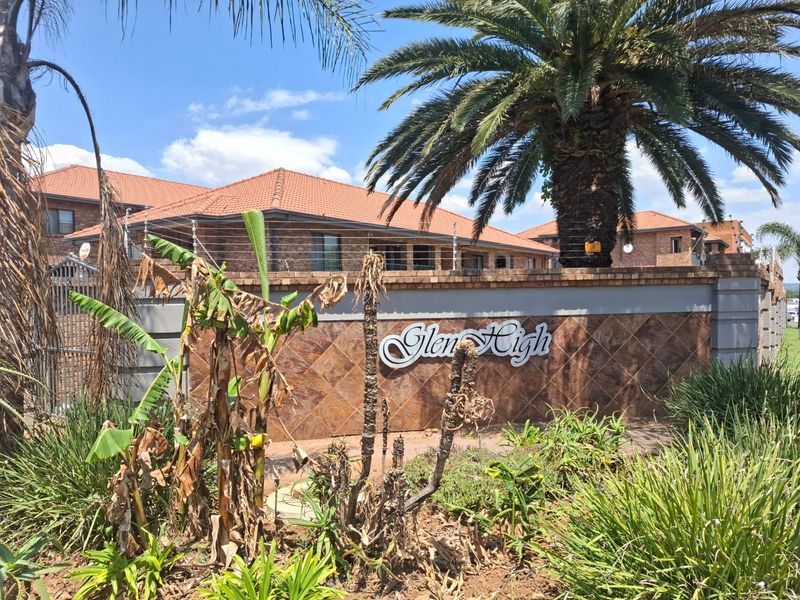 Front entrance view of the Glen High townhouse complex featuring a brick boundary wall, electric fencing, and established palm trees.