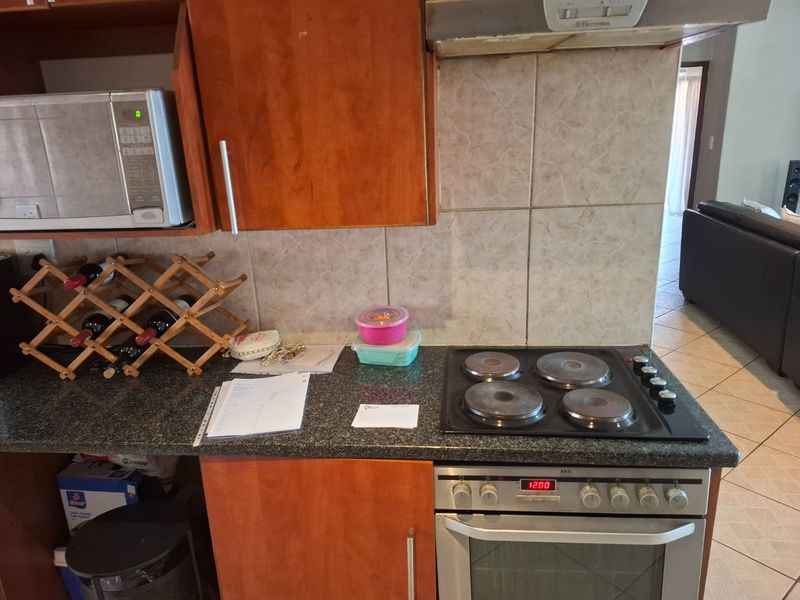 A functional kitchen area featuring wooden cabinetry, granite countertops, a built-in oven with an electric hob, and a tiled backsplash.