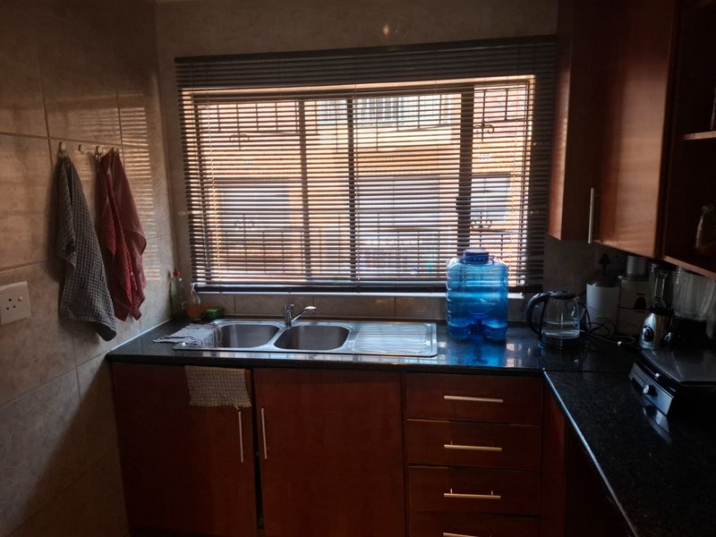 A functional kitchen area featuring dark granite countertops, wooden cabinetry, and a double bowl stainless steel sink set beneath a window with venetian blinds.