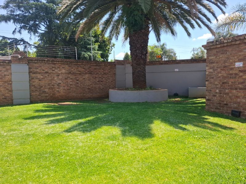 A well-maintained private garden area featuring a lush lawn, a mature palm tree in a raised planter, and secure brick boundary walls with electric fencing.