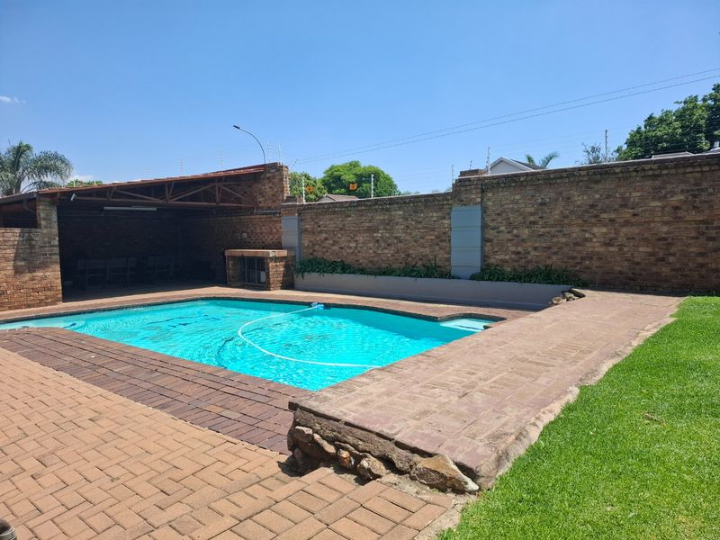 Outdoor pool area featuring a swimming pool, paved surround, built-in braai, and a covered patio area enclosed by a brick boundary wall.