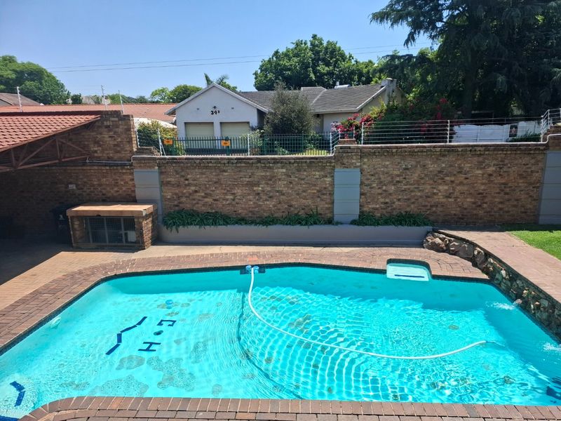 Outdoor pool area featuring a paved surround, built-in braai, and a brick boundary wall, providing a private space for relaxation and entertainment.