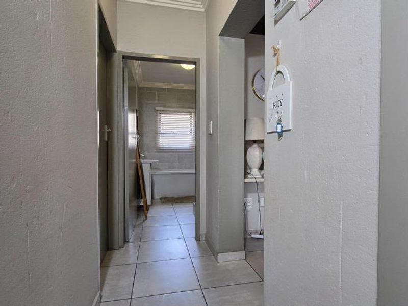 A neutral hallway with tiled flooring leading towards a bathroom, featuring clean lines and standard architectural finishes.