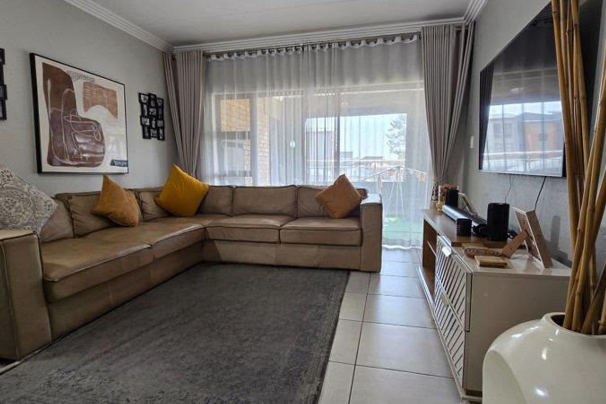 A comfortable living room featuring tiled flooring, crown molding, and a large sliding glass door that provides access to the outdoor area.