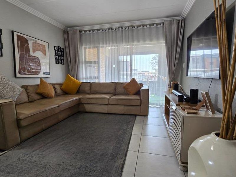 A comfortable living room featuring tiled flooring, crown molding, and a large sliding glass door that provides access to the outdoor area.