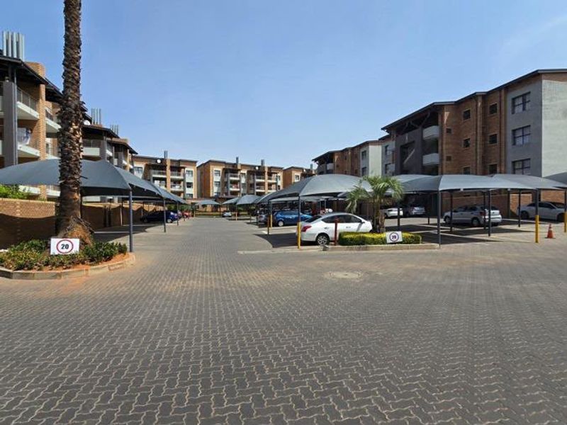 Exterior view of an apartment complex featuring paved parking areas with shade cloth carports and established brick building facades.