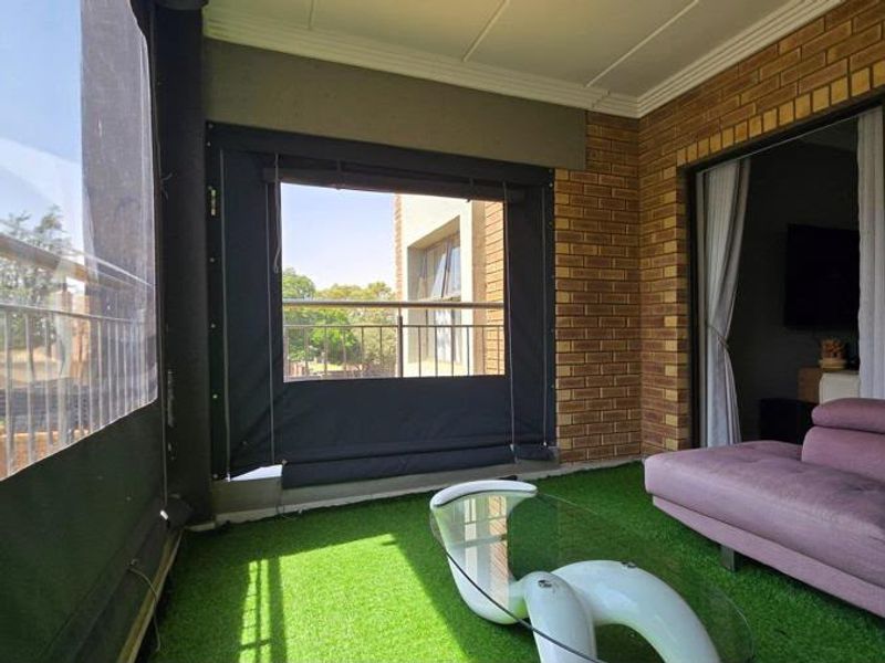 Enclosed balcony featuring brick wall finishes, artificial grass flooring, and protective outdoor roller blinds, providing a versatile semi-outdoor living space.