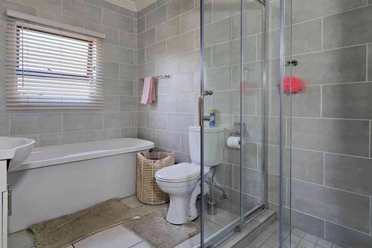 A modern bathroom featuring a bathtub, a separate glass-enclosed shower, and neutral grey wall tiling.