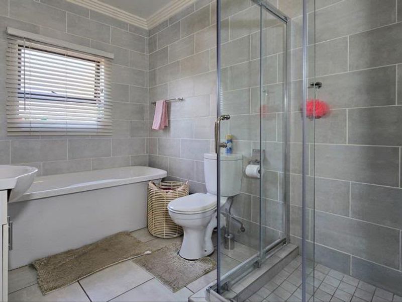 A modern bathroom featuring a bathtub, a separate glass-enclosed shower, and neutral grey wall tiling.