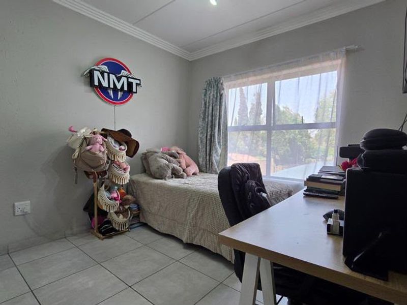 A functional bedroom featuring tiled flooring, a large window allowing natural light, and classic ceiling cornicing.