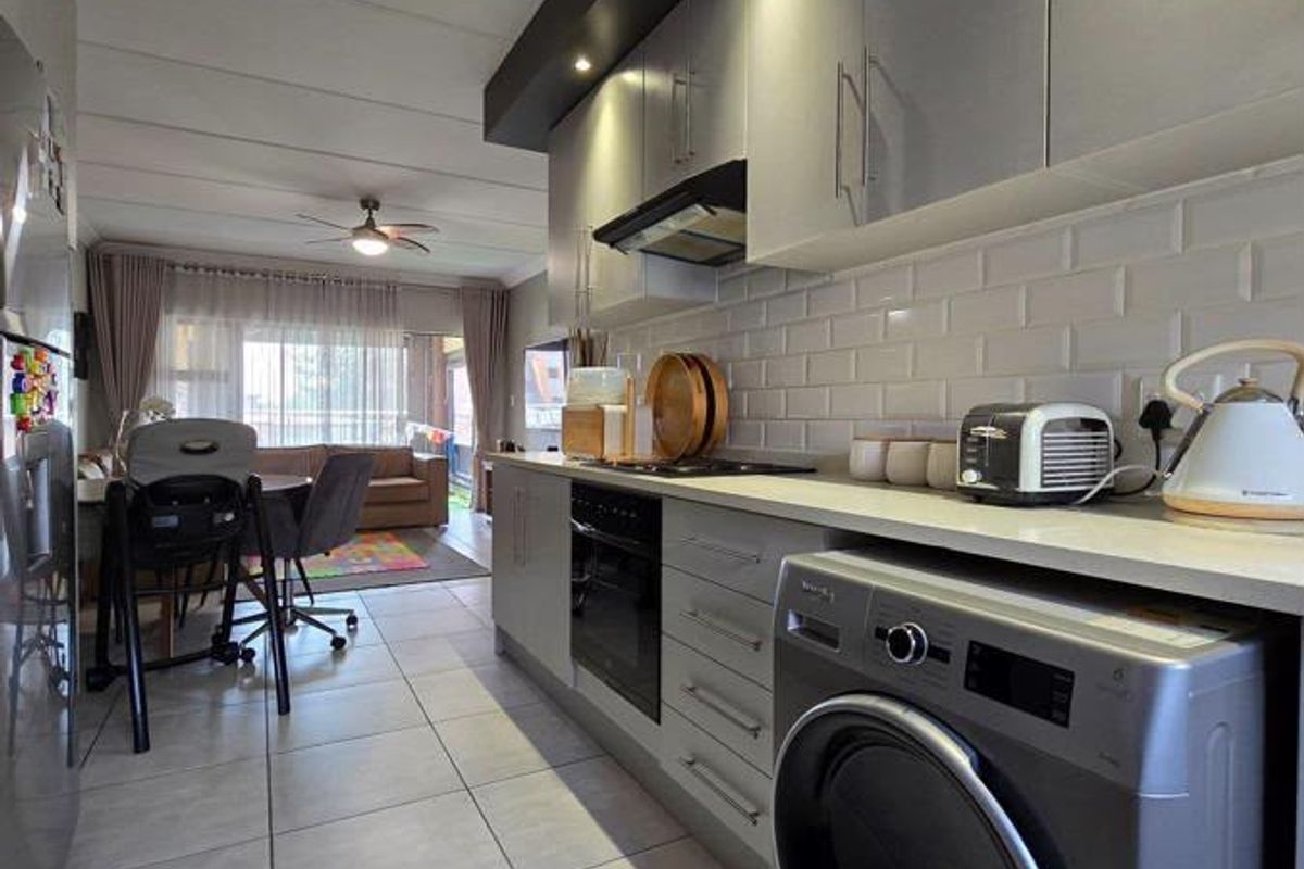 Modern open-plan kitchen and living area featuring sleek cabinetry, subway tile backsplash, built-in oven, and tiled flooring, creating a functional and contemporary living space.
