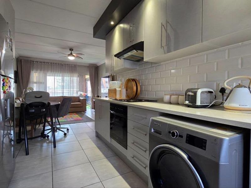 Modern open-plan kitchen and living area featuring sleek cabinetry, subway tile backsplash, built-in oven, and tiled flooring, creating a functional and contemporary living space.