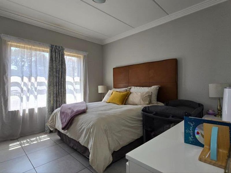 A well-lit bedroom featuring tiled flooring, crown molding, and a large window allowing for natural light.