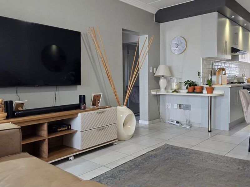 An open-plan living and kitchen area featuring tiled flooring, modern cabinetry, and a breakfast bar, creating a functional and connected living space.