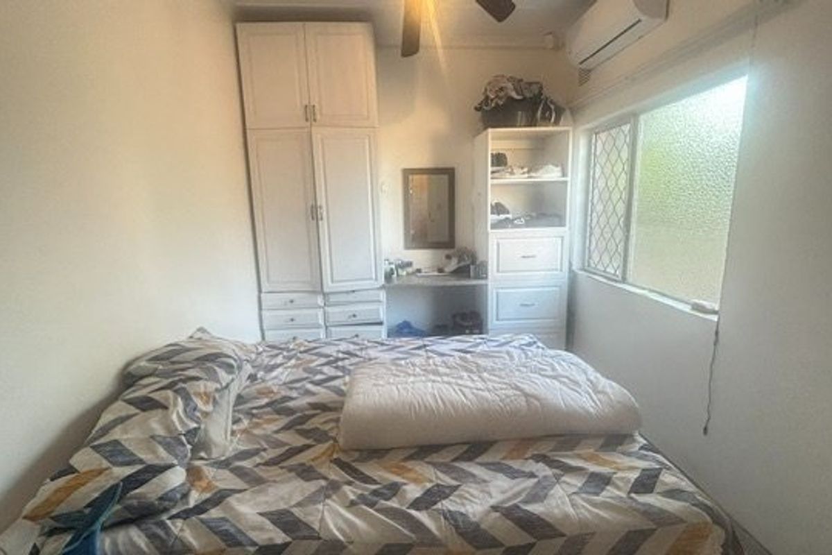 A functional bedroom featuring built-in cabinetry, a ceiling fan, and a wall-mounted air conditioning unit for climate control.
