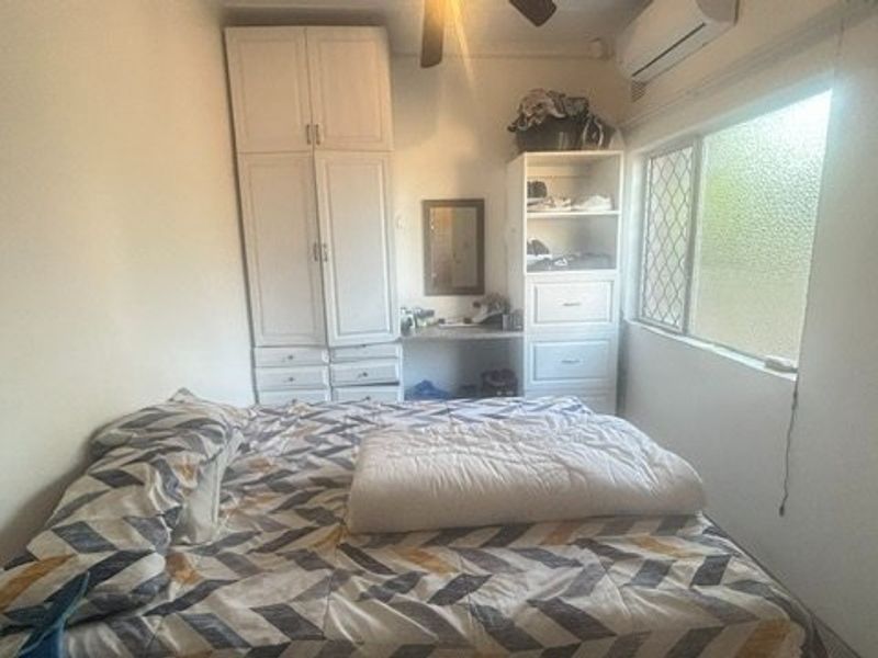 A functional bedroom featuring built-in cabinetry, a ceiling fan, and a wall-mounted air conditioning unit for climate control.