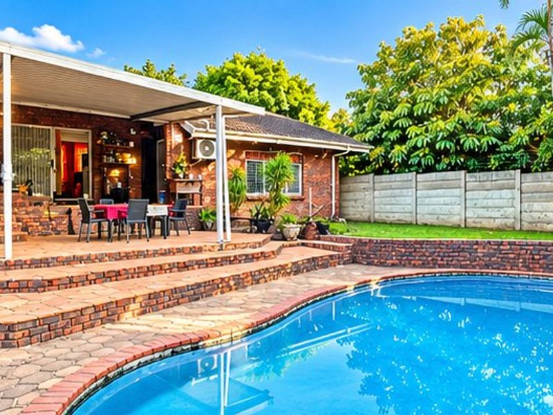 Outdoor entertainment area featuring a swimming pool, multi-level brick paved patio, and a covered veranda, set within a private garden with boundary walling.