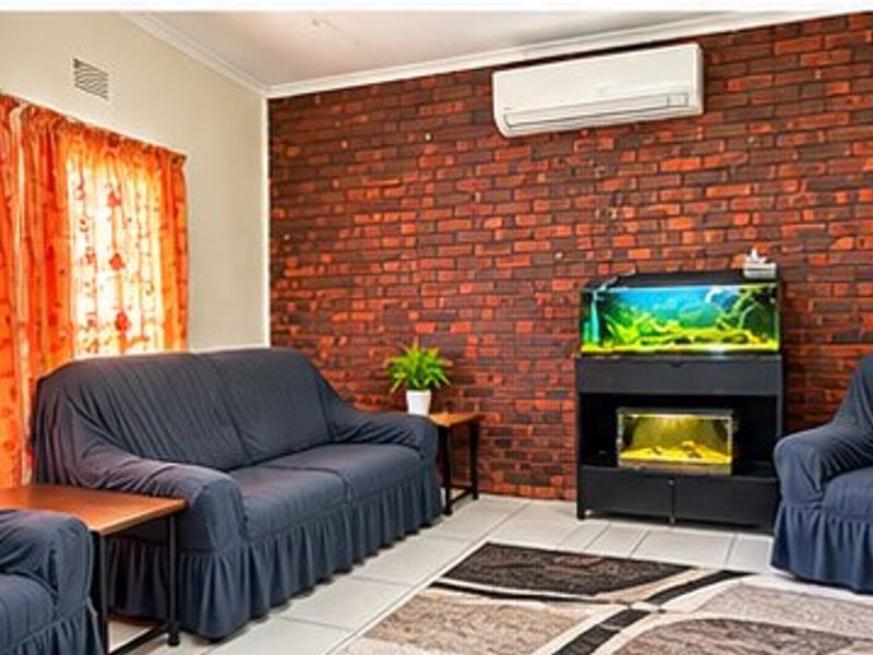 A living room featuring an exposed brick accent wall, tiled flooring, and a wall-mounted air conditioning unit.