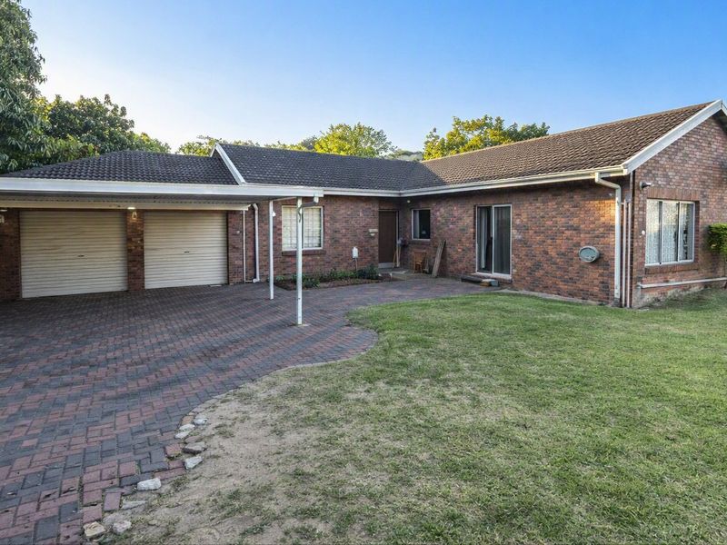 Front view of a single-story brick house featuring a double garage, attached carport, paved driveway, and a well-maintained lawn area.