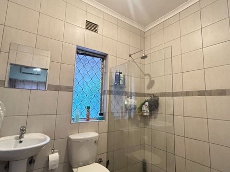 A functional bathroom featuring a pedestal basin, toilet, and a glass-enclosed shower with full-height wall tiling.