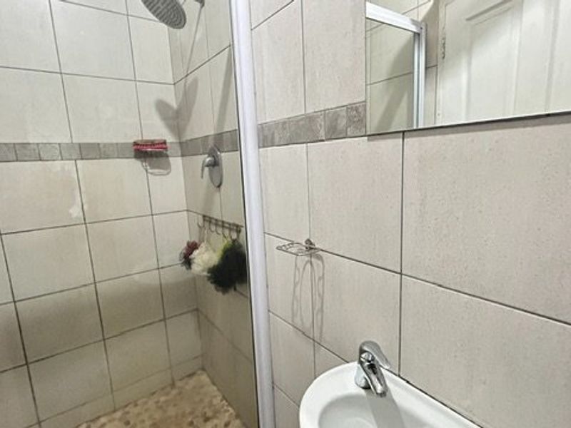 A functional bathroom featuring a tiled shower enclosure, pedestal basin, and wall-mounted mirror, presenting a standard layout with dated finishes.