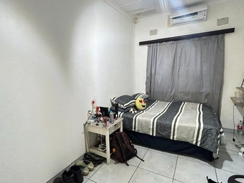 A bedroom featuring tiled flooring and a wall-mounted air conditioning unit, showing visible signs of water damage on the ceiling.