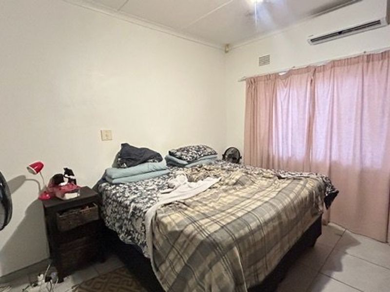 A functional bedroom featuring tiled flooring, an installed air conditioning unit, and curtain rails, providing a basic foundation for personalization.