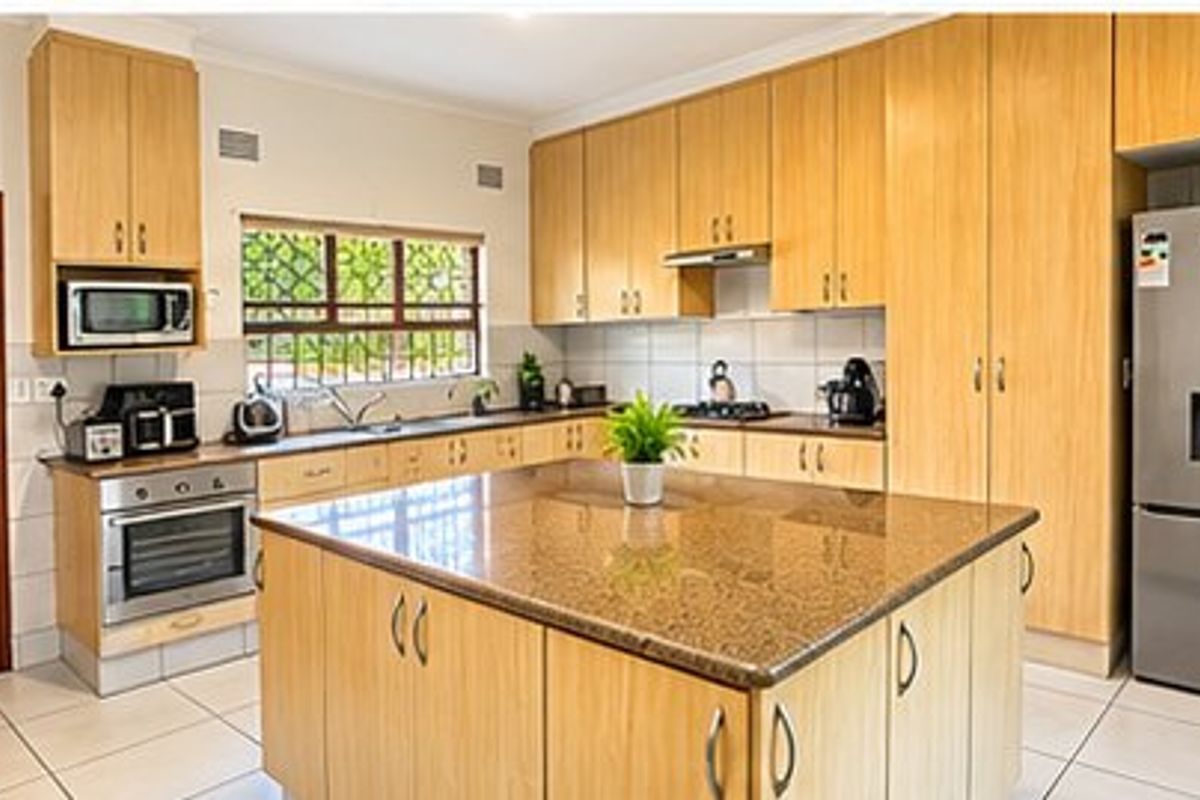 A functional kitchen featuring light wood cabinetry, granite countertops, a central island, and built-in appliances, finished with tiled flooring.