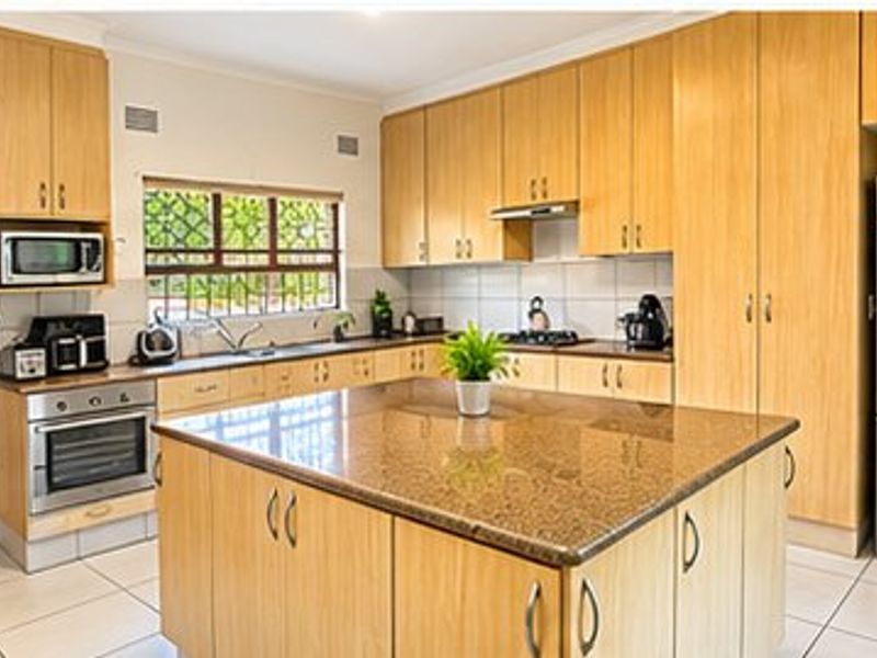 A functional kitchen featuring light wood cabinetry, granite countertops, a central island, and built-in appliances, finished with tiled flooring.