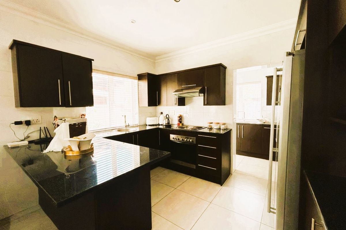 Modern kitchen featuring dark wood cabinetry, granite countertops, built-in oven, extractor fan, and tiled flooring, with an adjacent scullery area.