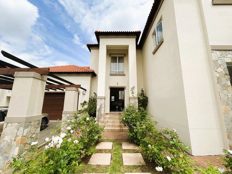 Front elevation of a townhouse featuring a tiled roof, stone cladding accents, a covered entrance with steps, and an attached garage with a pergola.