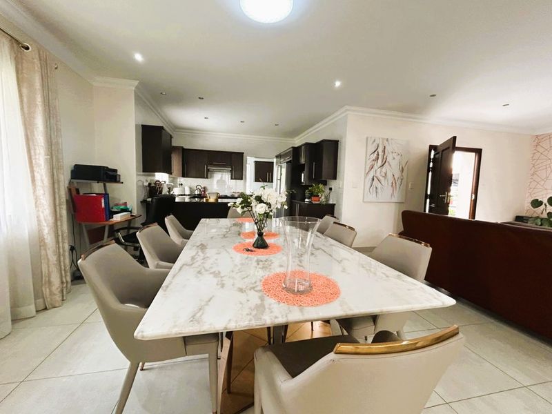 An open-plan dining area seamlessly connected to a modern kitchen, featuring tiled flooring, recessed lighting, and dark wood cabinetry.