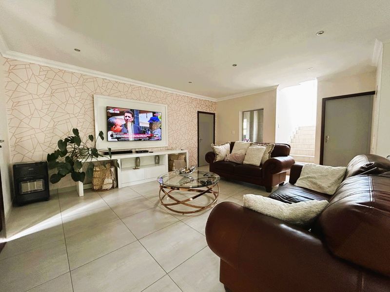 Spacious living room featuring tiled flooring, recessed downlights, and a feature wall with geometric wallpaper, leading to an internal staircase.