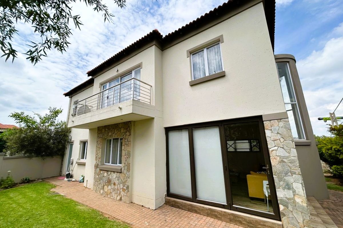 Rear view of the townhouse featuring stone cladding, a private balcony with stainless steel balustrade, sliding glass doors, and a paved patio area.