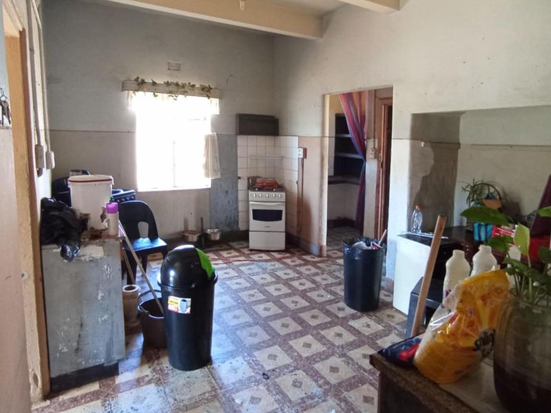 A dated kitchen area featuring tiled flooring, a freestanding stove, and tiled splashbacks, requiring significant renovation and cosmetic updates to improve its condition.