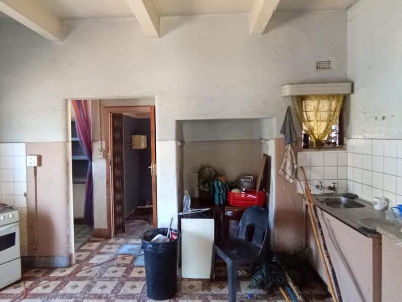 A dated kitchen featuring a freestanding stove, stainless steel sink, tiled splashbacks, and exposed ceiling beams, requiring significant renovation and cosmetic updates.