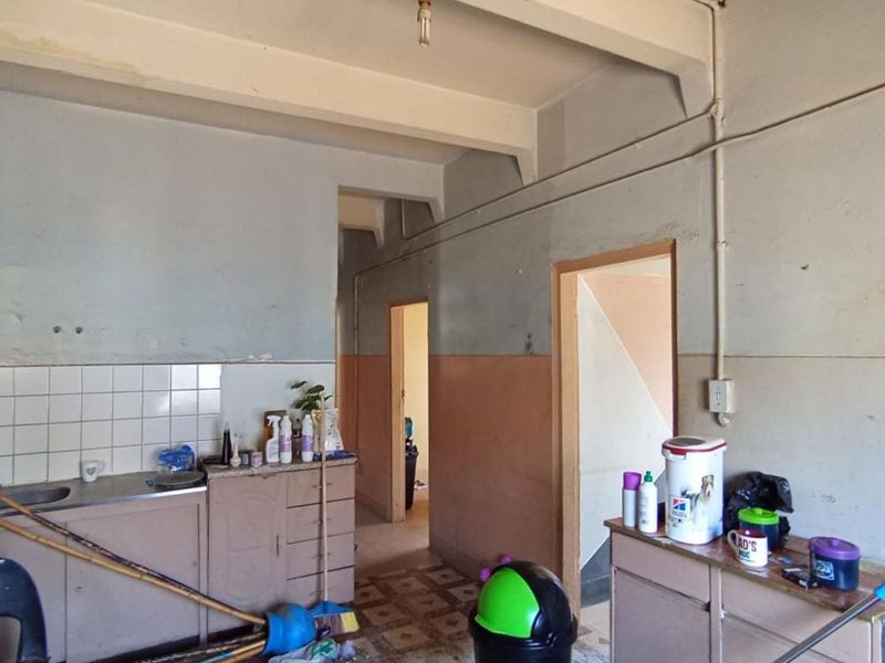 A dated kitchen area featuring built-in cabinetry, a stainless steel sink, and tiled splashbacks, requiring significant renovation and cosmetic updates.