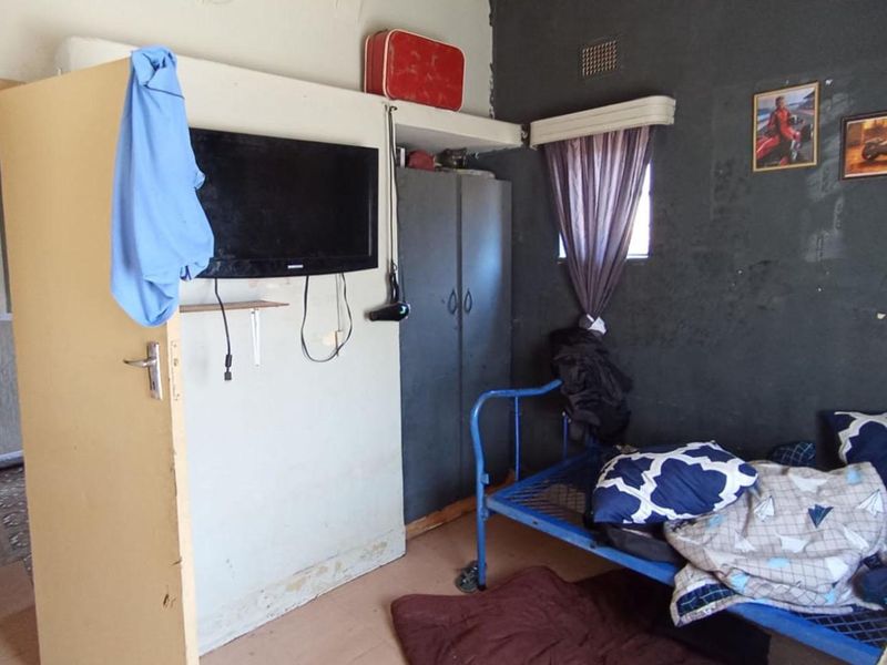 A bedroom featuring a built-in cupboard and ventilation grille, currently showing significant wear to wall finishes and flooring.