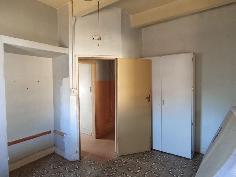 A vacant bedroom featuring built-in cupboards, shelving, and an exposed ceiling beam, requiring cosmetic updates and repairs to wall and floor finishes.