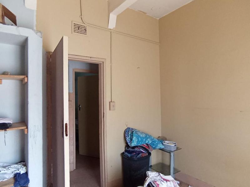 A bedroom featuring built-in shelving and a doorway leading to an adjacent room, requiring cosmetic updates to the walls and finishes.