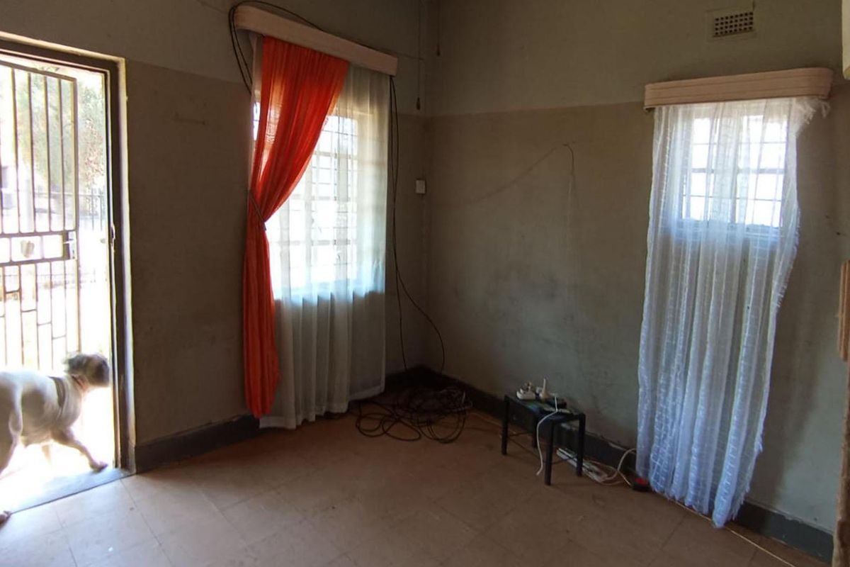An empty living room featuring tiled flooring, security gate access, and natural light through windows with existing curtain rails.