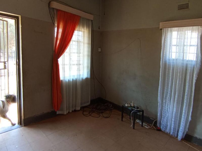An empty living room featuring tiled flooring, security gate access, and natural light through windows with existing curtain rails.