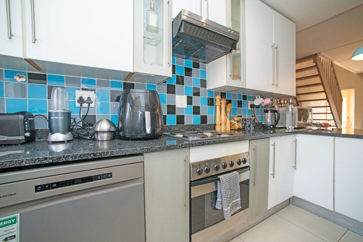 Modern kitchen featuring granite countertops, built-in oven, electric hob, extractor fan, and ample cabinetry with a vibrant tiled backsplash.