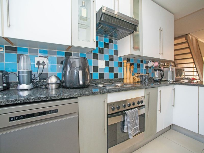 Modern kitchen featuring granite countertops, built-in oven, electric hob, extractor fan, and ample cabinetry with a vibrant tiled backsplash.